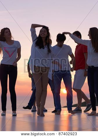 group of happy young people dancing and have fun on party in modern home bacony with sunset and ocean in background