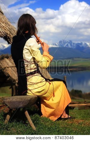 l girl in a historical costume playing her flute in an open landscape with a lake