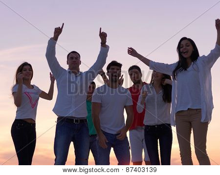 group of happy young people dancing and have fun on party in modern home bacony with sunset and ocean in background