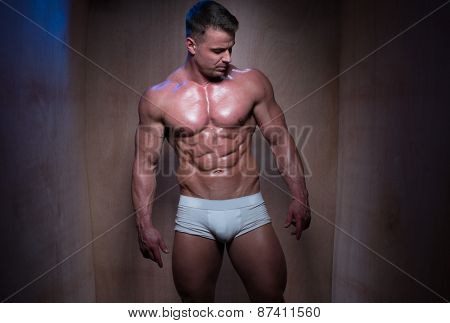 Muscular Man Wearing Tight White Boxer Shorts Looking Down and To the Side in Dimly Lit Room