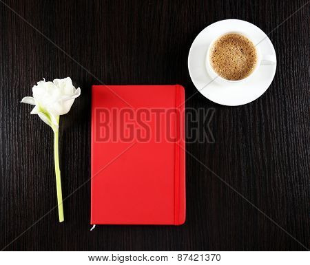 Cup of coffee with notebook and fresh flower on wooden table background