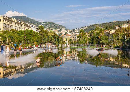 NICE, FRANCE - OCTOBER 2, 2014: Children playing in fountain on Promenade du Paillon reflecting the city and surrounding hills.