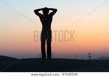 The man silhouette at sunset in desert with hands behind his head