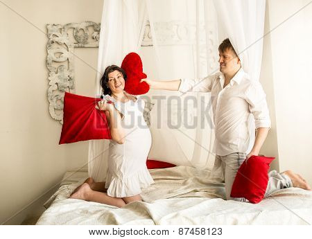 Pregnant Woman Having Pillow Fight With Husband On Bed With Baldachin