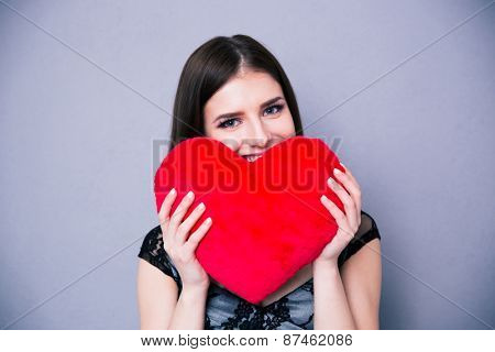 Happy beautiful woman holding red heart over gray background and looking at camera