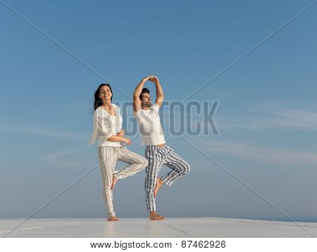 young couple practicing yoga at sunset in modern home terace with ocean and sunset in background