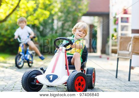 Little Kid Boy Driving Pedal Car In Summer Garden