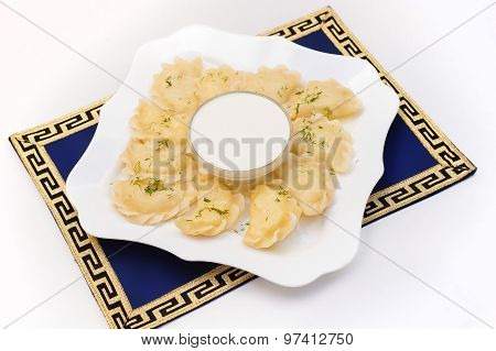 Varenyky, dumplings or pirogi, with sour cream and greens on white plate