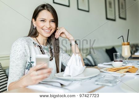 Beautiful Smiling Lady Sitting In A Restaurant And Holding Her Phone