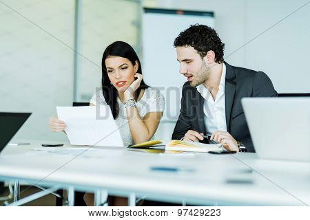 Young Businesswoman And A Businessman Looking At A Paper While Sitting At A Office Desk