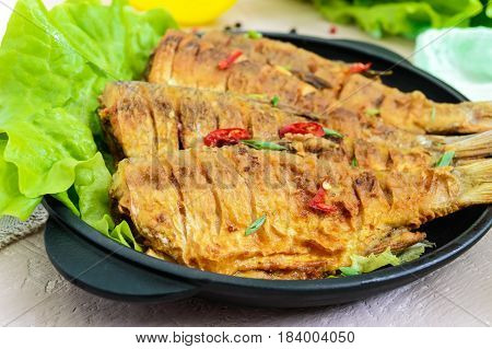 Fried fish carp (sazan) on a cast-iron frying pan with lettuce leaves on a light background. Close up