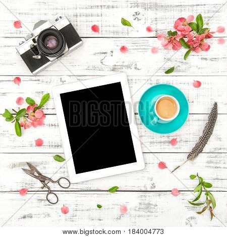 Tablet PC vintage photo camera coffee pink flowers on white wooden background. Spring flat lay