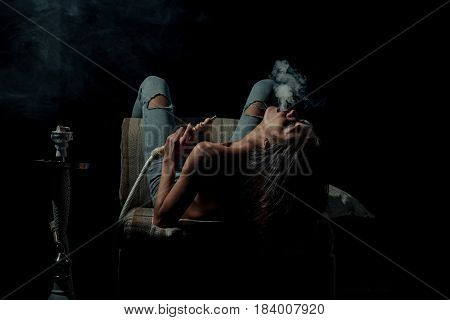 arabic tradition naked girl smoking hookah pretty woman with sexy back and body in jeans sitting on eastern chair with shisha bong or kalian on black background