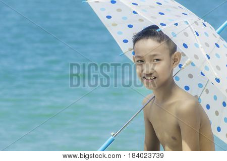 Happy little boy with umbella on the beach at blue sky background.