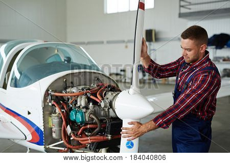 Portrait of modern aircraft engineer repairing jet plane in hangar, disassembling engine and fixing propeller motors