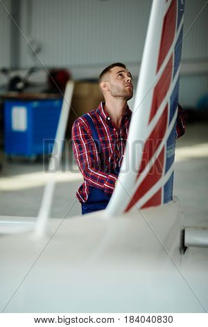 Airplane service crew working on preflight maintenance: Portrait of handsome mechanic inspecting fuselage of jet plane in hangar