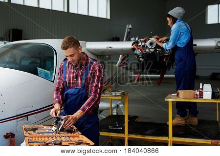 Airplane service crew working on preflight maintenance:  two young mechanics, man and woman, repairing jet plane in hangar