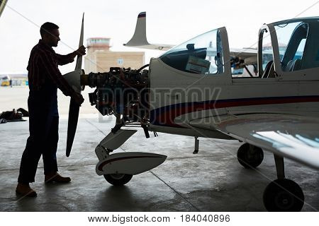 Dark silhouette of aircraft mechanic assembling jet plane in maintenance hangar
