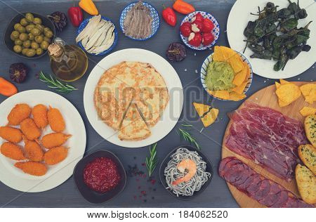 Table with spanish tapas - jamon, croquetes, guacamole and olives, top view, picnic table, retro toned