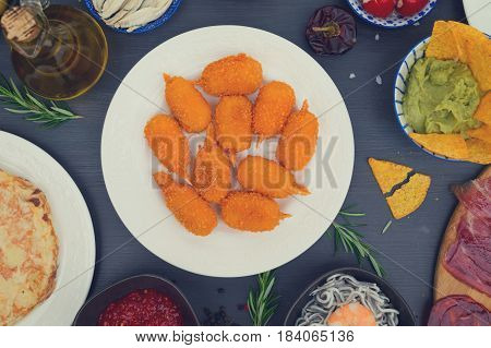 Table with spanish tapas - jamon, croquetes, guacamole and olives, top view, picnic table, retro toned