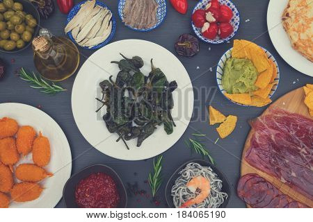 Table with spanish tapas - green grilled padron peppers, jamon, croquetes, guacamole and olives, top view, picnic table, retro toned