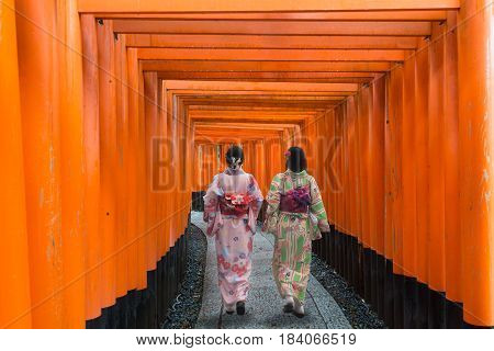 Two geishas among red wooden Tori Gate at Fushimi Inari Shrine in Kyoto Japan. Women wearing traditional japanese kimono in Kyoto Japan.