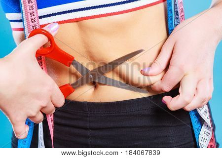 Weight gain diet liposuction concept. Woman with measure tapes pinches in the fat at the waist holding scissors cut fold skin