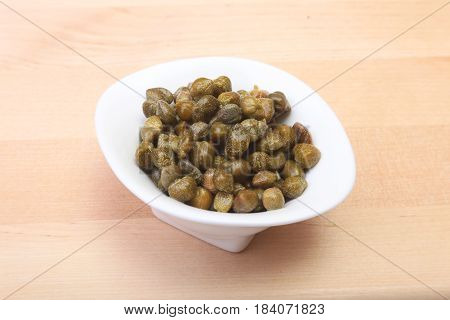 bowl with fresh capers on wooden table.