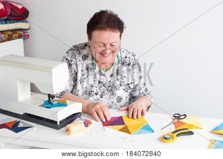 needlework and quilting in the workshop of a tailor woman - elderly smiling women put on the desktop the pieces of colored tissue, lay next to the scissors, buttons, pins and thread, rotary cutters