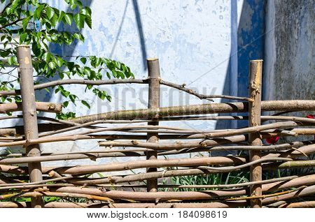 A braided wooden fence made of thin old branches in the countryside against the backdrop of an old house
