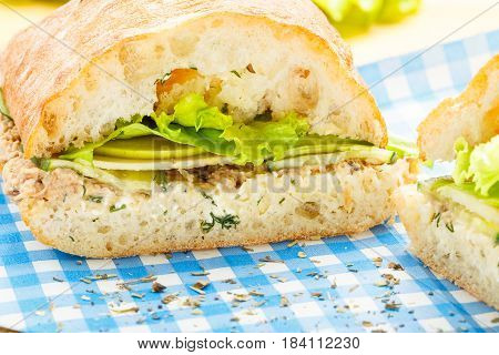 Large ciabatta sandwich with tuna, green, apple and cucumber lying on a blue napkin and a wooden board