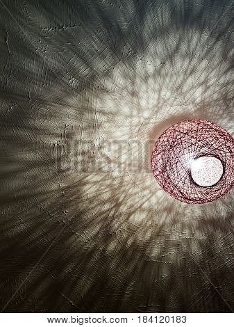 A lightshade throws abstract shadow patterns onto a white ceiling