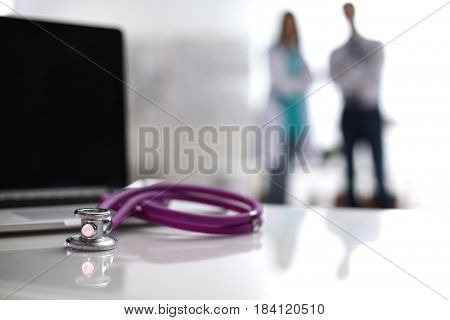 Laptop and stethoscope on the desk doctors standing in the background.