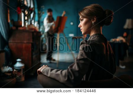Female poseur, painter against easel on background