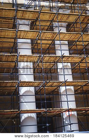 Metal scaffolding with wooden decking built around a historic building with columns for restoration work and renovation of the facade. Construction works. Building construction.