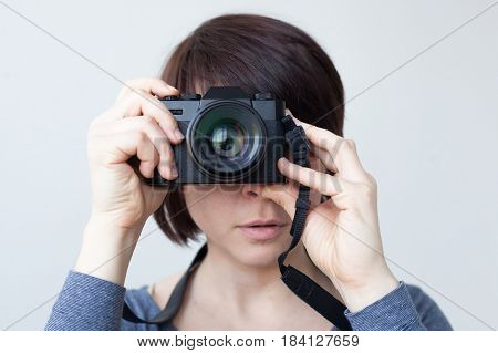 A girl is holding a camera by her face. The lens looks like a big eye. Hobby with photography