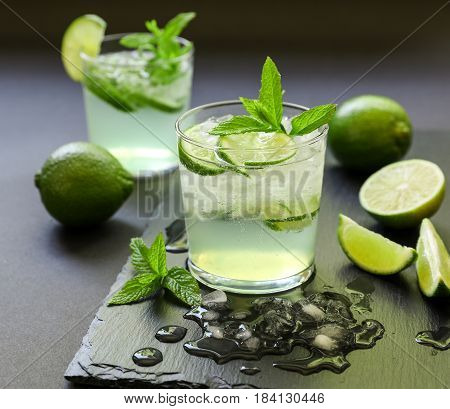 Cold cocktail with lemon liqueur, lime, tonic, ice in two glasses or mojito cocktail on dark background. Close-up.