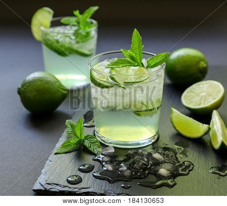 Cold cocktail with lemon liqueur, lime, tonic, ice in two glasses or mojito cocktail on dark background. Close-up.