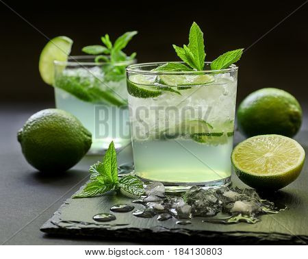 Cold cocktail with lemon liqueur, lime, tonic, ice in two glasses or mojito cocktail on dark background. Close-up.
