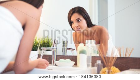 Young woman washing her face with clean water in bathroom.