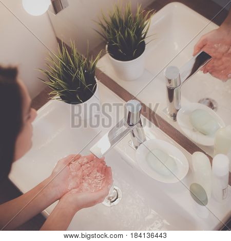 Young woman washing her face with clean water in bathroom.