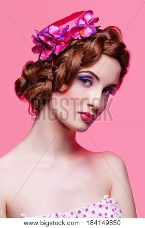 Beautiful young woman with red braided hair, bright make-up and small fancy hat over pink background. Pin up style. Copy space.