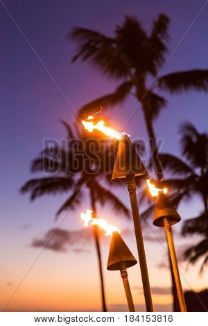 Hawaii sunset with lit tiki torches. Hawaiian icon, lights burning at dusk at beach resort or restaurants for outdoor lighting and decoration, cozy atmosphere.