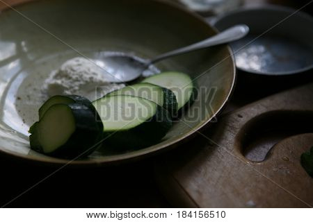 still life with slices of green zucchini, flour, spoon, сopper bowl and a wooden cutting board in close-up
