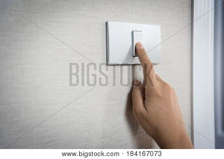 Close up hand turning on or off on grey light switch with texture background. Copy space.