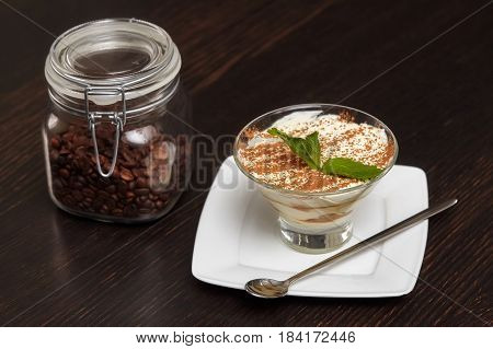 Tiramisu creme cake dessert in glass with mint leaves on black wooden background