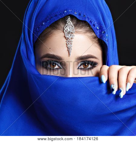 Gorgeous Young East Woman face portrait in hijab. Beauty Model Girl with bright eyebrows, perfect make-up, touching her face. Traditional. Isolated on black background. Smokey.Jewelry on her face. Studio