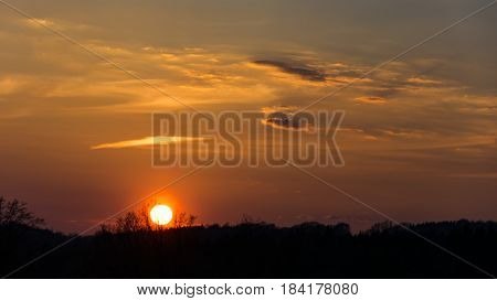 Red sky with few clouds during sunset over the hill. Silhouette of meadow. Strong sun is near above the horizon.