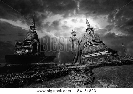 Black and white view of statue of Buddha between great pagoda with beautiful sky within Wat Sa Si at Sukhothai Historical Park Thailand