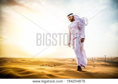 Arabian man walking in the desert at sunrise
